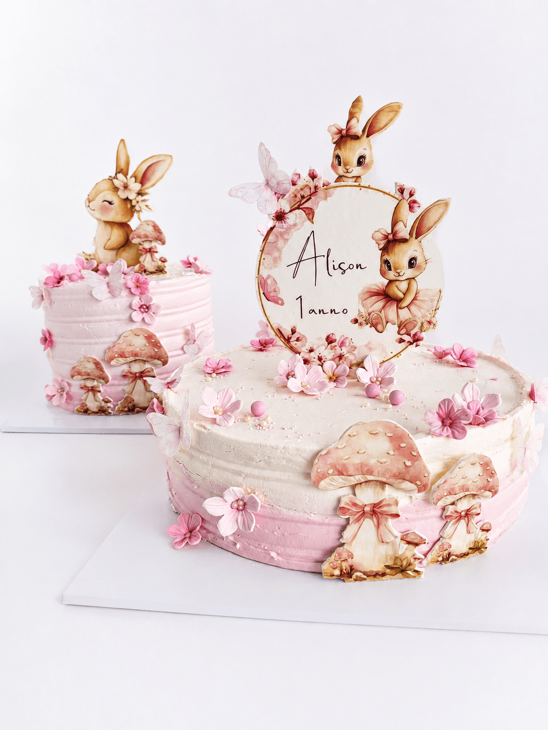 Due torte rosa con coniglietti, funghi, fiori e farfalle